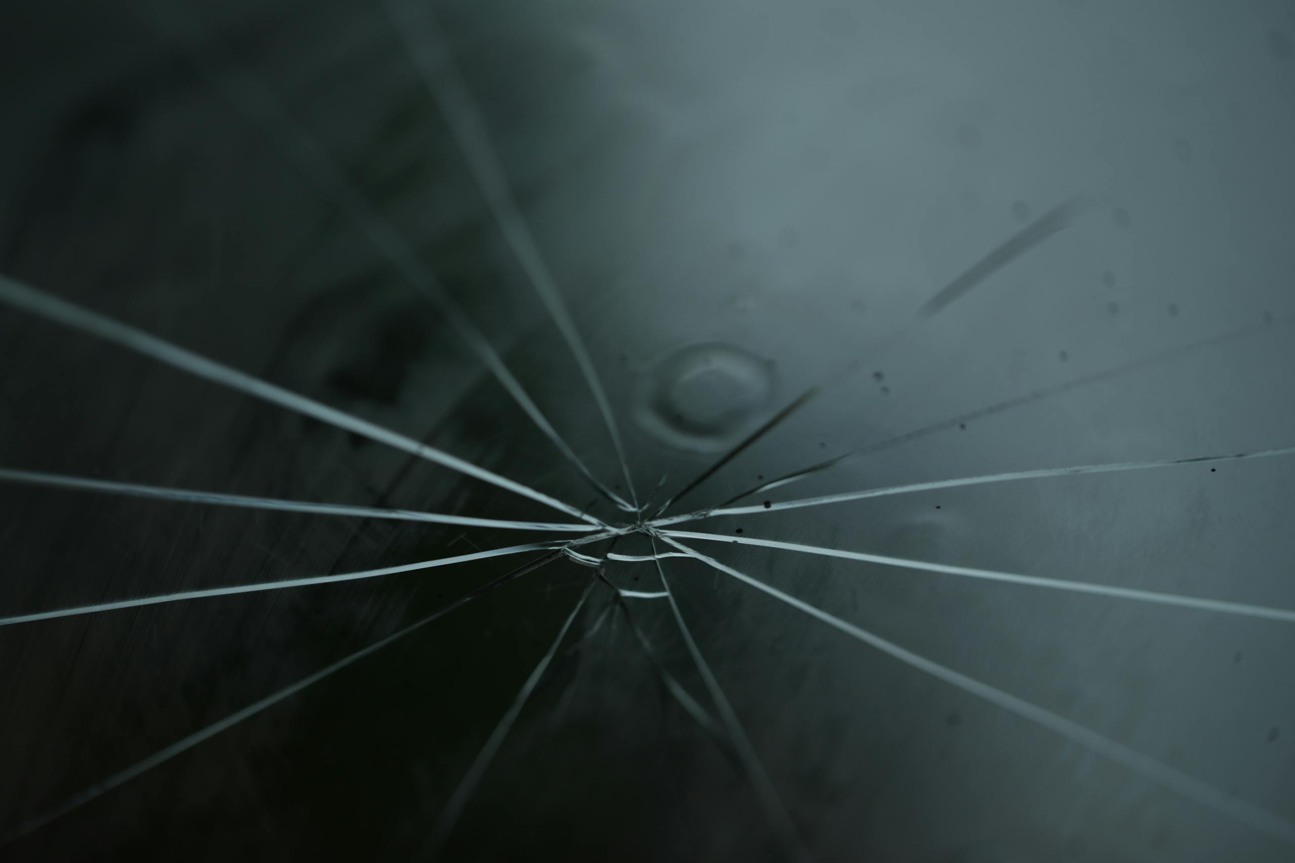 A detailed shot of cracked glass with radiating lines on a moody background.