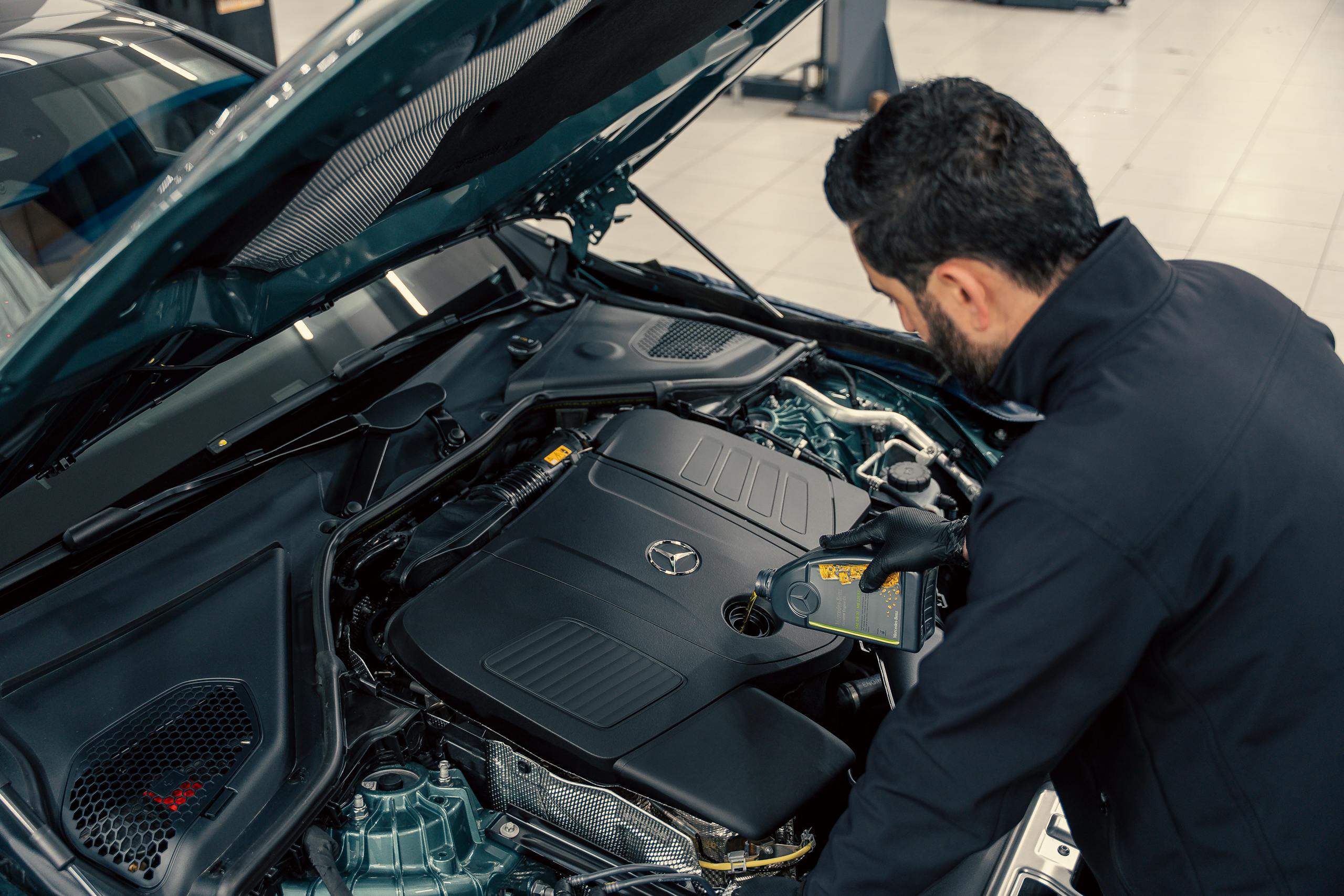 Mechanic inspecting and filling engine oil in a car at an indoor service center.